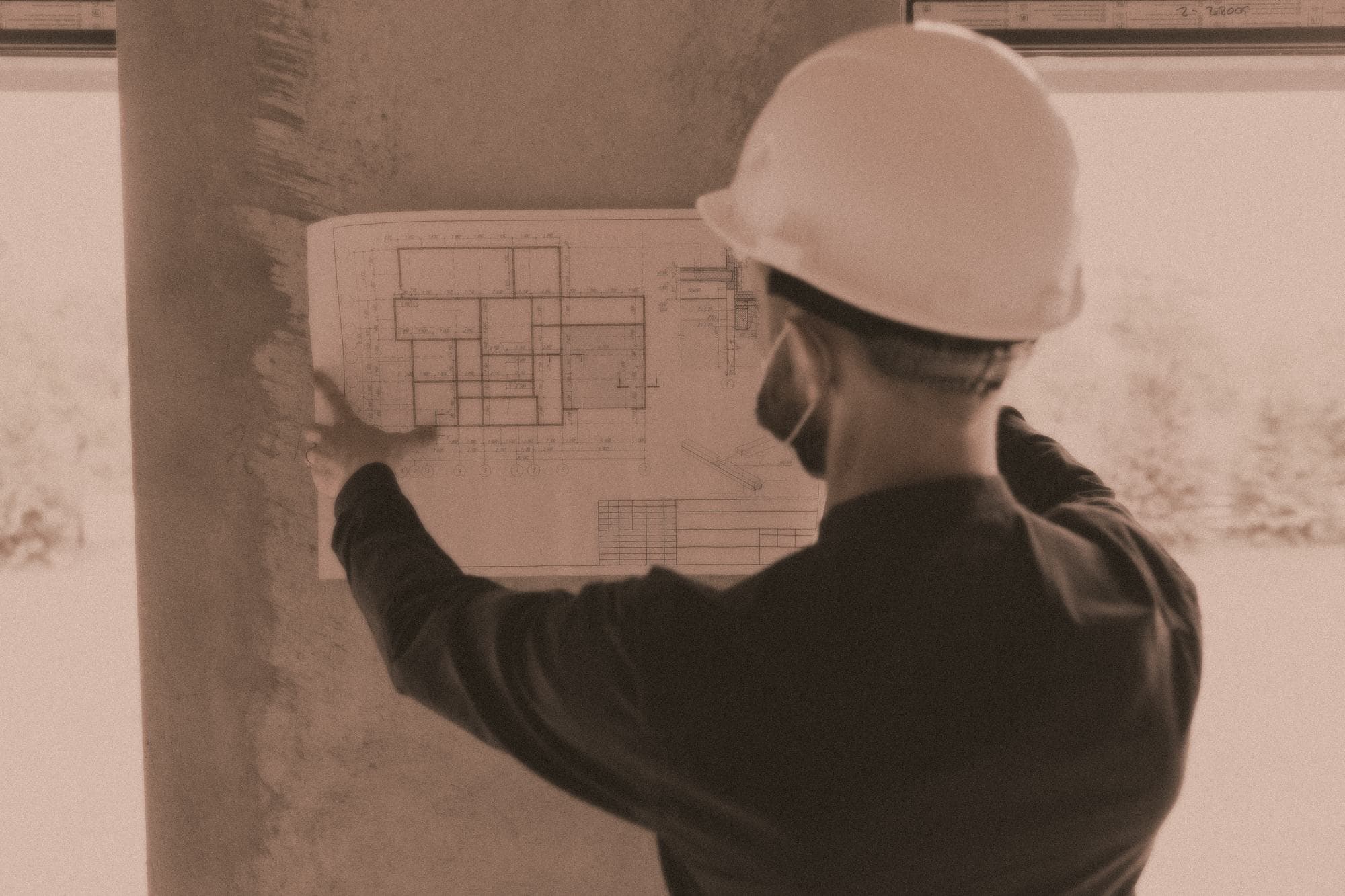 An engineer in a hard hat holding a building floor plan up against a concrete column