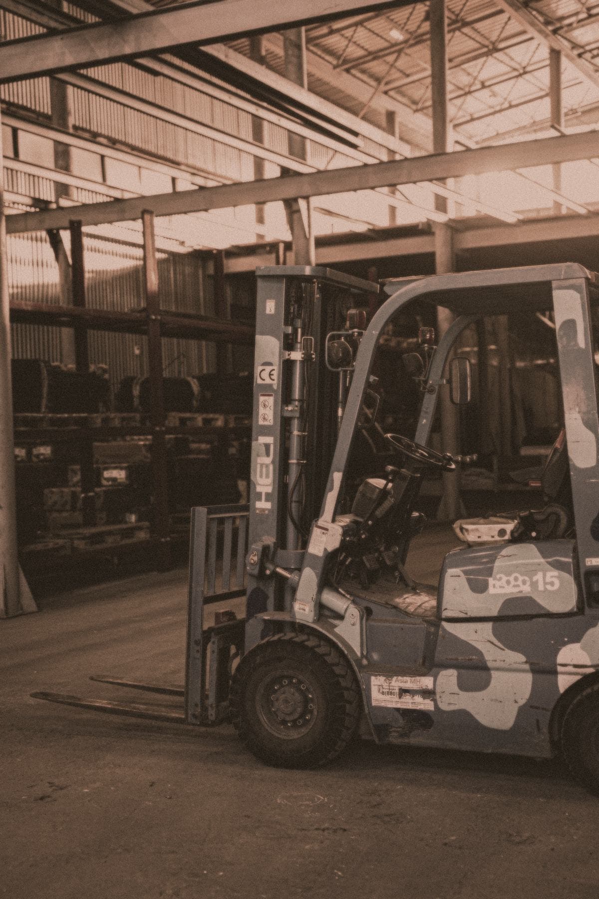 A forklift truck parked in a warehouse beneath racking and roof lights