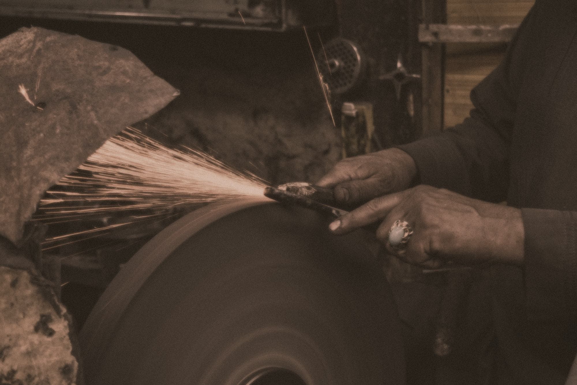 A machinist's hands guiding metal against a grinding wheel, sparks fanning out