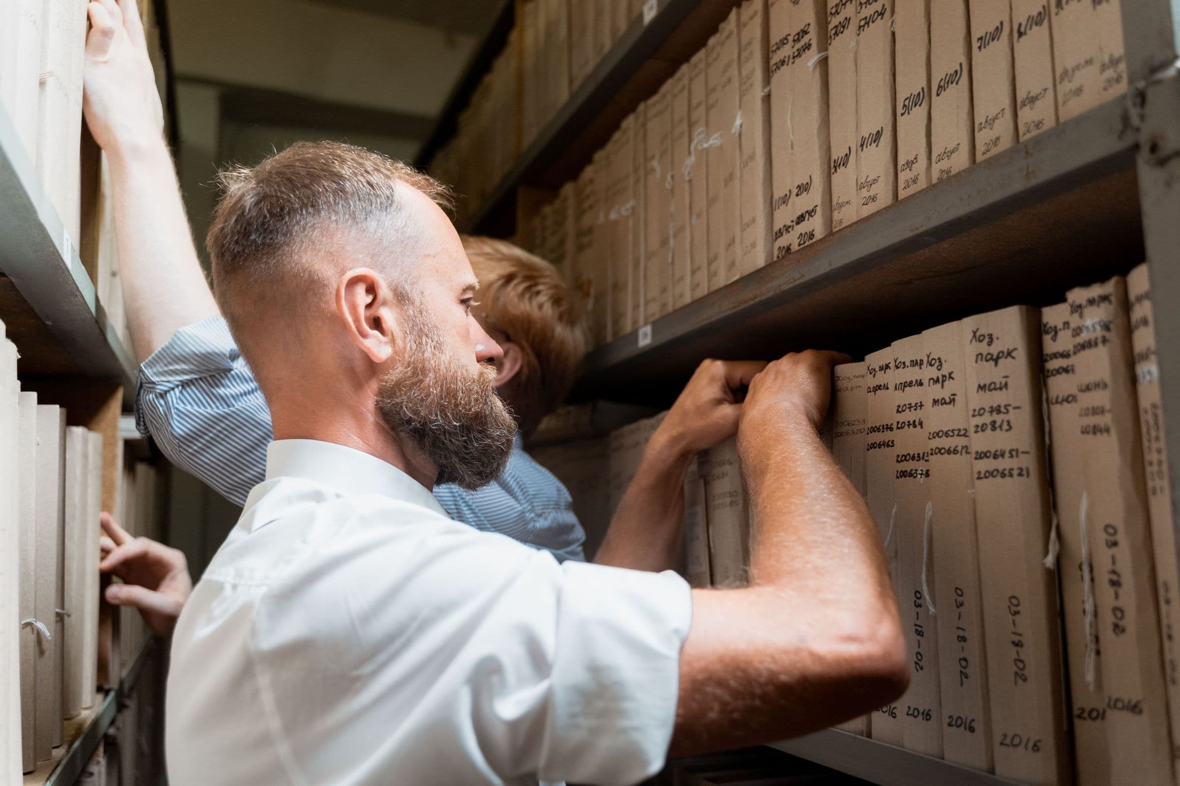 An archivist reaching for labelled record boxes on tall archive shelving